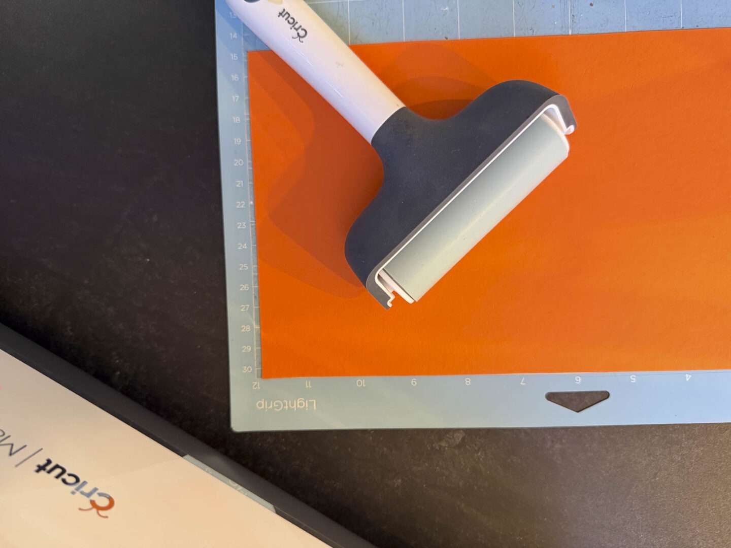 Orangefarbenen Tonkarton mit einer Rolle auf der blauen LightGrip-Schneidmatte des Plotters andrücken.