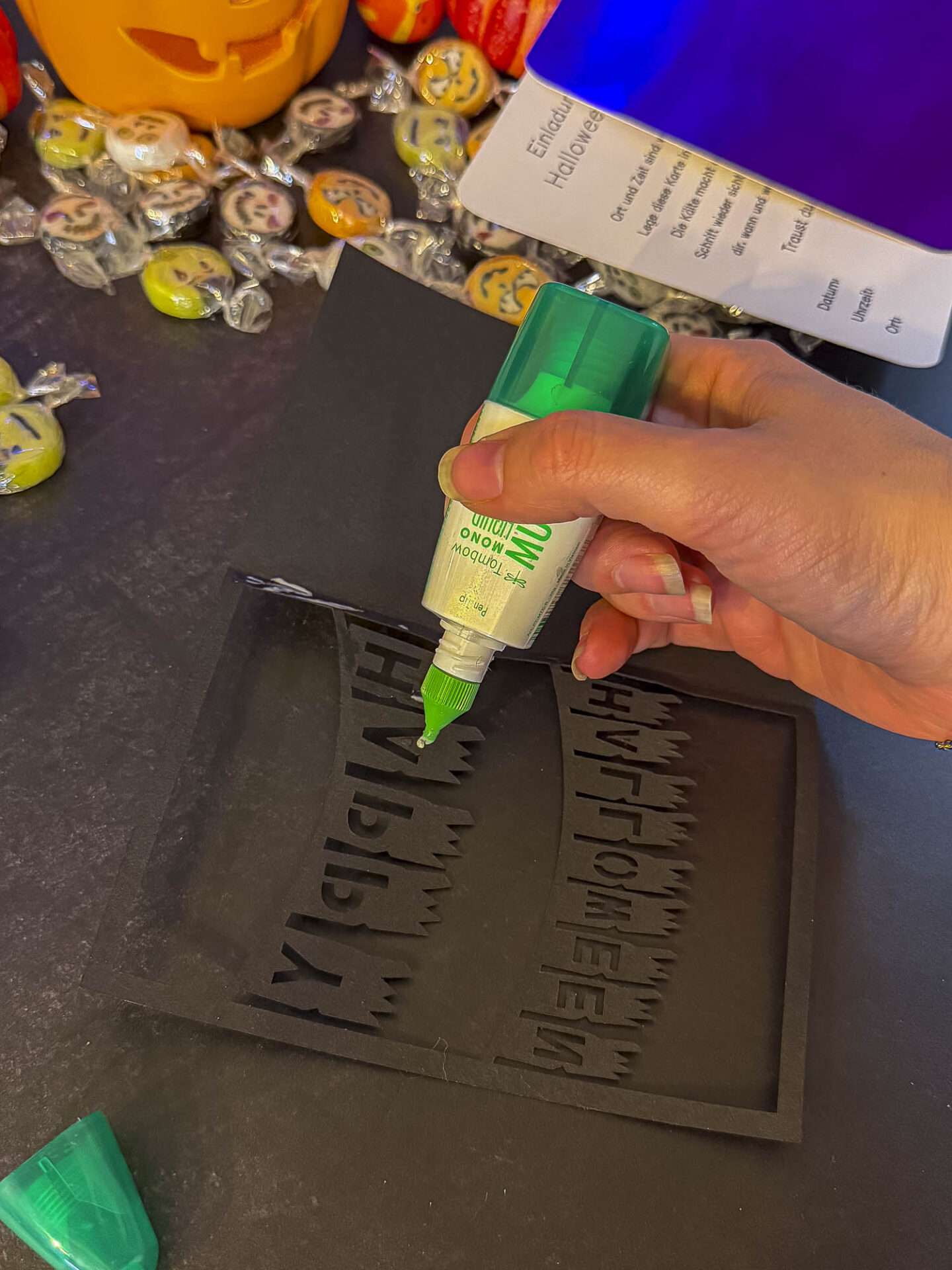 Flüssigkleber auf die Rückseite des ausgeschnittenen Schriftzugs der Halloween-Klappkarte auftragen.